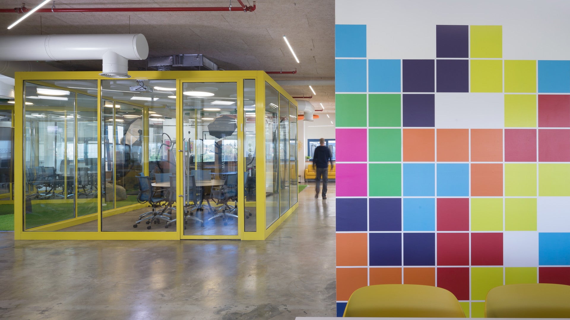 Modern office space at Foto Master with glass-walled yellow meeting room and colorful pixel-style wall art.