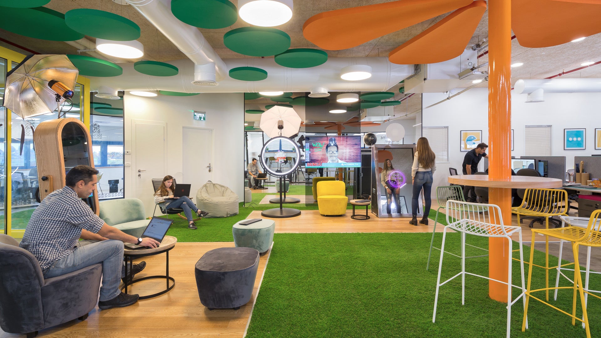 Foto Master employees working and relaxing in colorful open space with mirror booths, turf flooring, and playful ceiling decor.