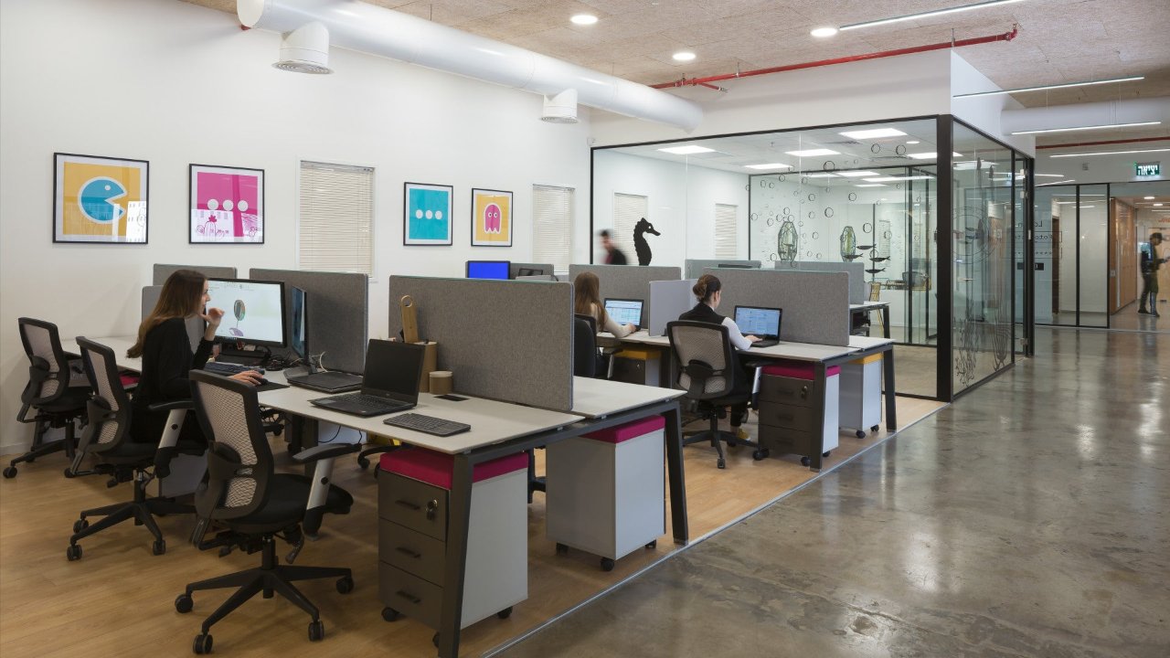 Open workspace at Foto Master with employees working at cubicles, pop-art wall prints, and adjacent glass meeting room.