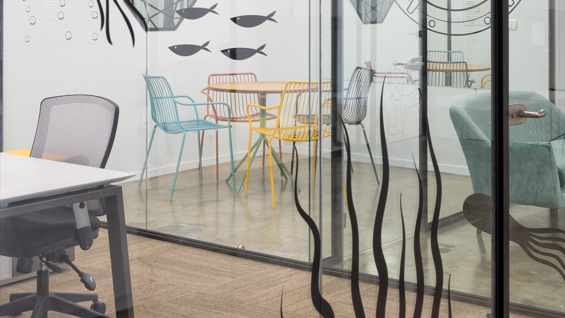 Glass meeting room at Foto Master with colorful chairs, fish wall art, and playful underwater-themed glass decals.